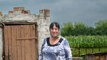 A woman poses for a photo in front of a building destroyed by the war in Ukraine.